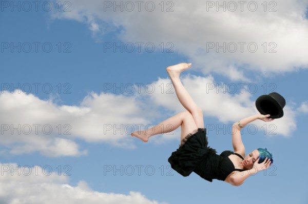 A beautiful young actress dancer wearing a top hat flying through the sky or falling through the air