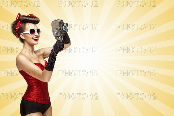 Retro photo of a glamorous pin up girl with an old vintage cinema 8mm camera shooting a film on colourful abstract cartoon style background
