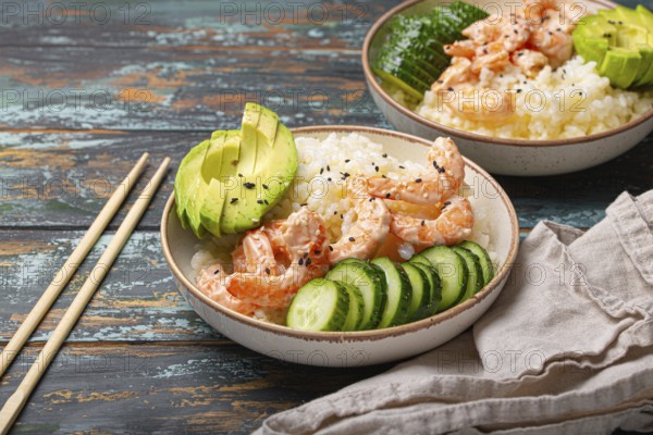 White ceramic bowl with rice, shrimps, avocado, vegetables and sesame seeds and chopsticks on colourful rustic wooden background front view. Healthy asian style poke bowl
