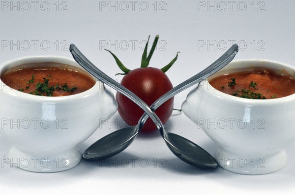 Cream of tomato soup in a white bowl with a spoon and a cherry tomato