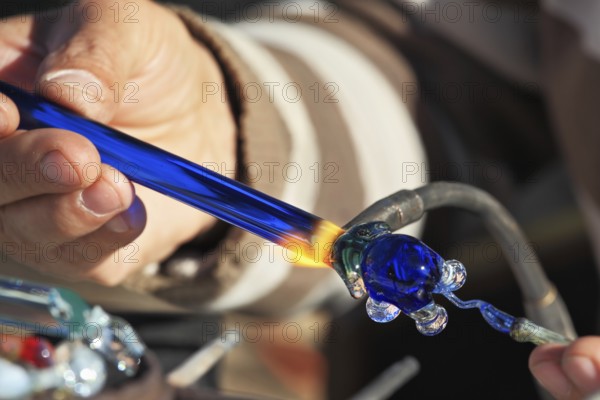 Delicate work of the glass blower. On a photo hands of the master are visible. The Artist-glass blower produces a graceful tiny figure of an elephant from color glass