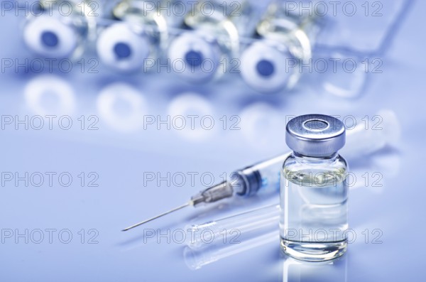 Single use syringe for injection treatment on medical table with vials of liquid drug doses flu shots at background. Vaccination or immunization care concept