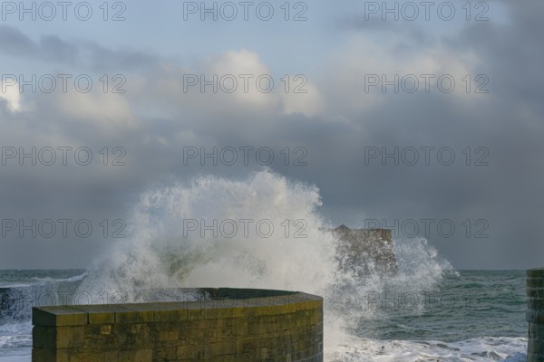 Waves crash against a stone pier wall, with a cloudy sky above and the ocean extending into the distance, Saint-Malo, Ille-et-Vilaine, France, Europe