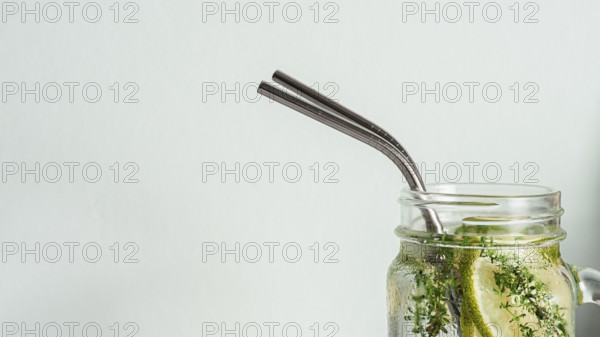 Cold drink in mason jar with metal straw on white background. Lemonade or detox water with lime and thyme in glass jar with copy space for text or design. Recyclable straws, zero waste concept. Banner