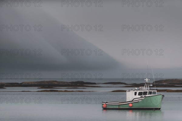 A commercial fishing boat sits tied to its mooring with dramatic clouds above, behind it are shoals leading to the Atlantic Ocean in Lunenburg, Nova Scotia, Canada, North America