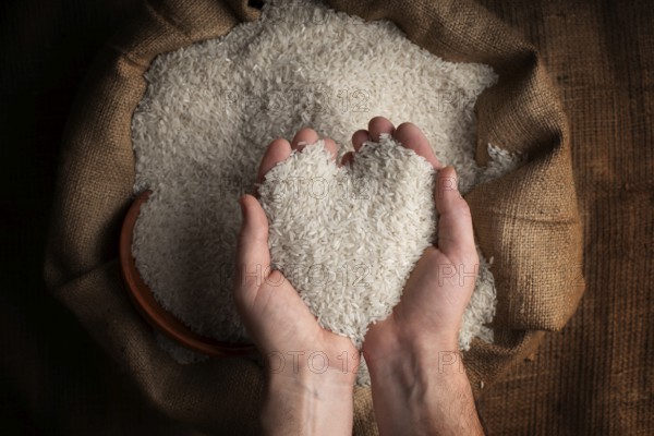 Human hands in shape of heart holding handful of rice over burlap sack