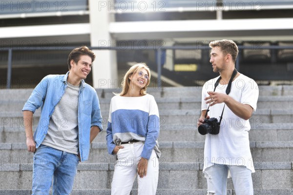Three happy friends talking taking a conversation on the street in a sunny day with buildings in the background