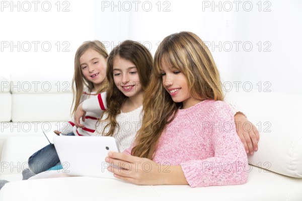 Three kid sister friends girls group playing together with tablet pc on white sofa