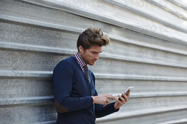 Young businessman texting smartphone phone on the street metal fence