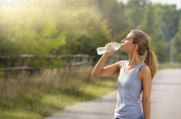Young woman drink water while jogging outdoors