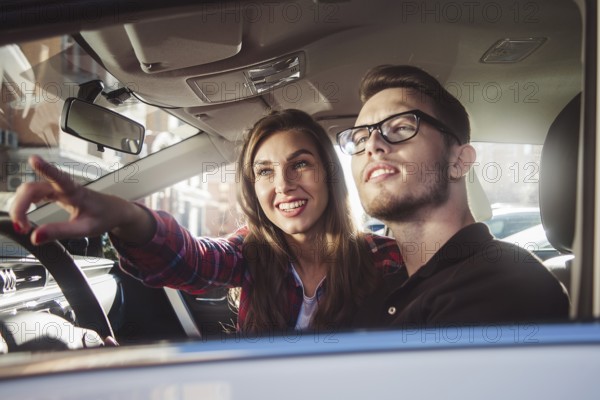 Enjoying travel. Beautiful young couple sitting on the front passenger seats and smiling while handsome man driving a car