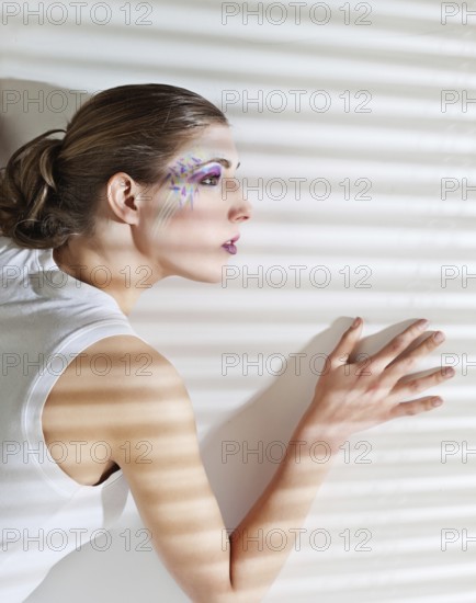 Pretty young woman lean lit by bright sunlight coming through the blinds, Belgium, Europe