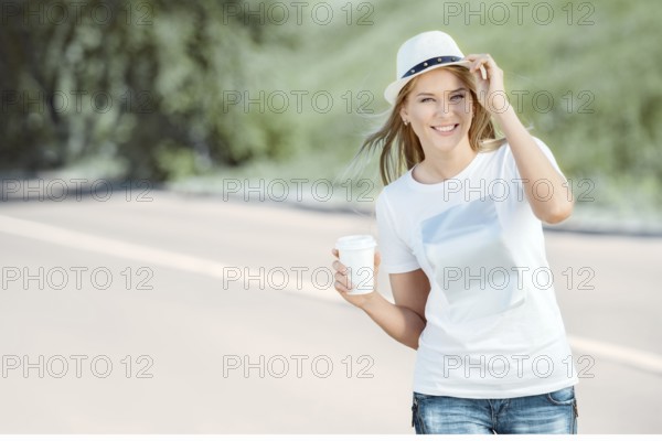 Beautiful young woman walking with a disposable coffee cup, drinking coffee and smiling against the backdrop of urban nature
