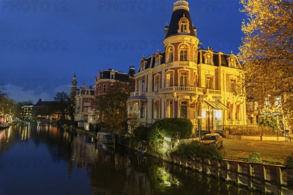 A romantically lit scene with historic buildings along a canal in the evening, Amsterdam, Netherlands