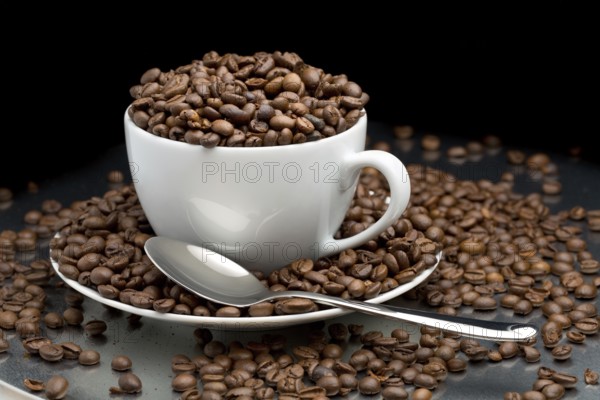 Cup and saucer full of coffee beans with a spoon on a black background