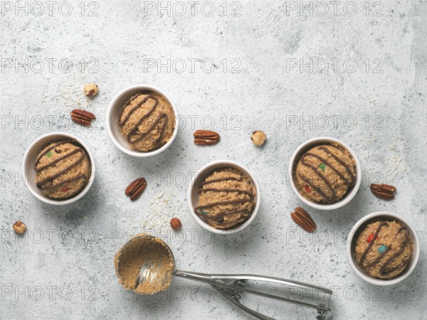 Safe-to-eat raw monster cookie dough in small portion bowl, ice cream scoop and nuts on gray cement background. Ideas and recipes for kids and toddlers meal. Top view or flat-lay. Copy space for text