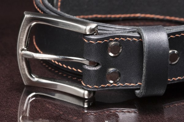 Black leather belt with a metal buckle on a dark background close-up