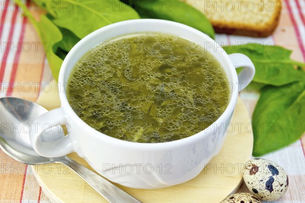 Soup of green nettles, sorrel, spinach, rhubarb leaves on a round wooden board, bread, quail eggs, spoon on a cloth background