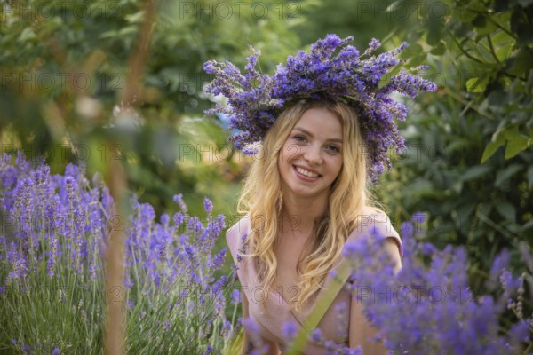 Blonde woman in wreath near lavender bushes at the garden