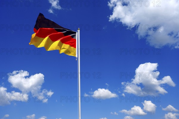 The flag of Germany flutters in the wind in a blue sky with white clouds
