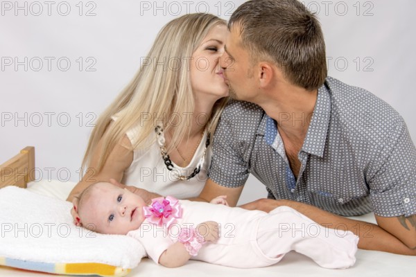 Young parents Mom and Dad sit at the crib, the crib on his back lying on the two-month girl