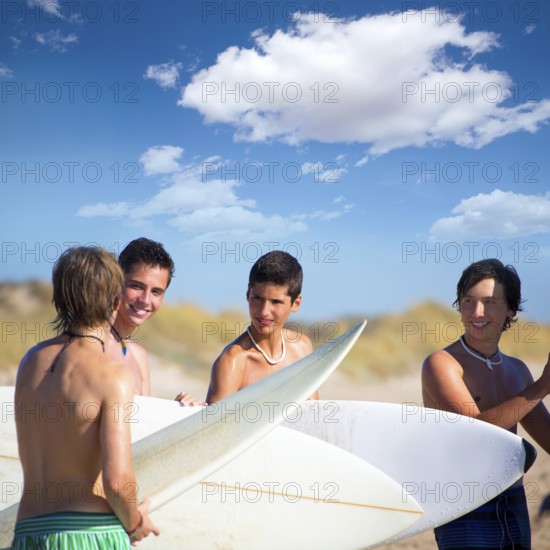 Surfer teen boys talking on beach shore holding surfboards