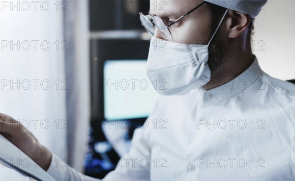 Healthcare worker wearing mask and glasses, carefully examining a document in a clinical setting