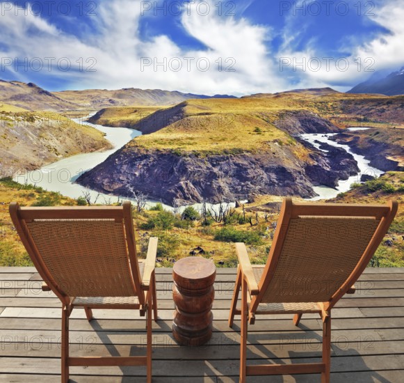 Two wooden chairs - on a wooden platform. The comfortable place to enjoy the beauty of the landscape. The magnificent national park Torres del Paine in Chile. Picturesque river bends a horseshoe of hills orange
