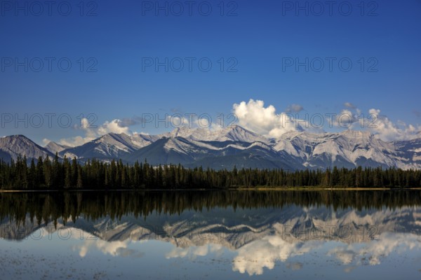 The Canadian Rockies and bright blue sky are reflected in a lake near Canmore, Alberta, Canada, North America