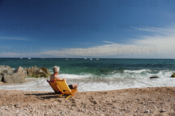 Elderly man at orange and yellow chairs on the tranquil beach
