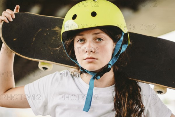 Schoolgirl after lessons at skateboarding practice in outdoor skate park. Stylish and beautiful caucasian girl with skateboard on a half pipe ramp in a skatepark. Teenager skater girl with skate deck
