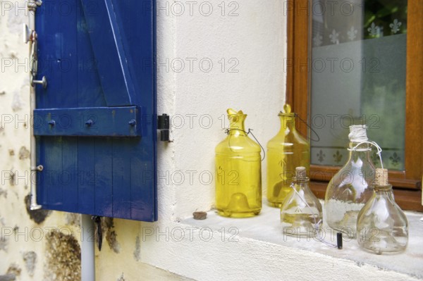 Still life with old glass bottles in window with blue shutters in France