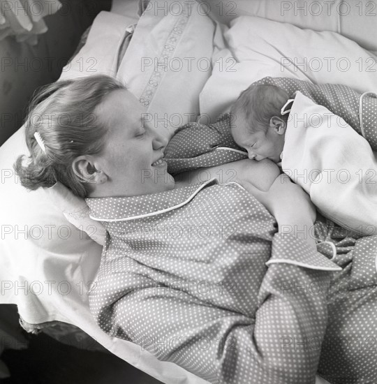 1950s mother nursing her baby. A young woman breastfeeding her baby while lying in bed at home. Sweden 1951 Neg CV/24