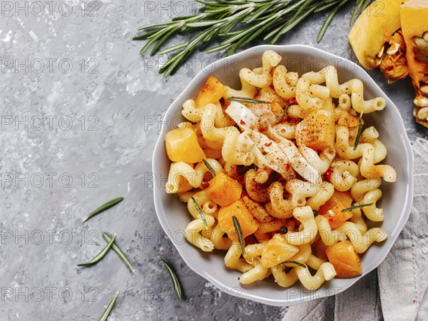 Fusilli pasta with pumpkin, rosemary and brie cheese. Idea recipe pasta. Vegetarian food. Homemade pasta dish in gray bowl over gray concrete background. Copy space. Top view or flat lay