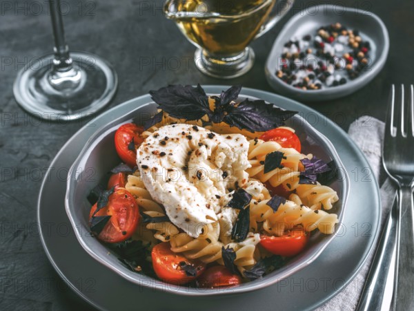Tasty italian fusilli pasta with cherry, mozarella or buratta cheese and fresh basil. Dish with pasta on dark tabletop. Copy space. Healthy food concept and recipe idea