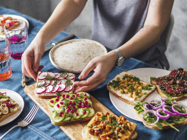 Female hands on dinning table. Young woman eat vegetarian toast. Vegan veggies sandwiches on dinning table