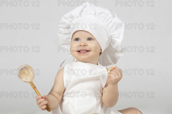 Child cooking. Beautiful little girl in cooking clothes with a big spoon. The child is one year old. Funny baby laughs. Little cook. The concept of cooking food