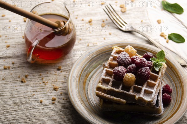 Belgian waffles served with raspberries and mint leaf dusted with powdered sugar on white wooden kitchen table with syrup aside. Selective focus