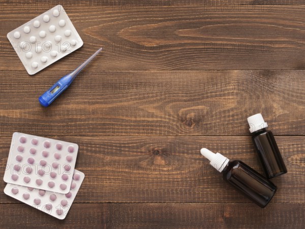Medications or tablets and drops and electronic thermometer on a dark wooden background with copy space. Flat lay or top view