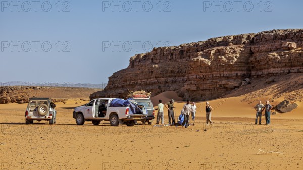 Off-road vehicle and people in a sunny desert landscape with impressive rock formations, Off-road vehicle driving through the dry desert, a tree in the foreground, With off-road vehicle through the Sahara desert in Algeria