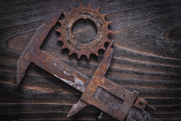 Rusted age-old measuring calipers with gear wheel on vintage dark wooden background construction concept
