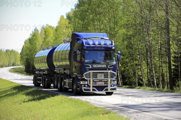 TENHOLA, FINLAND, JUNE 4, 2017: Dark blue Scania R580 tank truck with bull bar of Tomppa Tuomisto Ky moves along highway in light and shadow of a rural landscape in South of Finland at summer