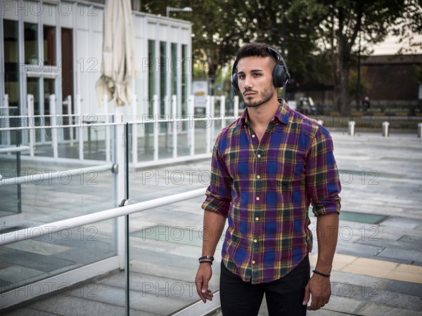 Young attractive man in city setting listening to music with headphones, walking