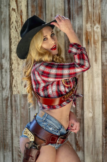 A confident, beautiful blonde woman in classic cowboy attire stands tall, posing with a gleaming pistol on her hip and a rifle resting across her shoulder. Her smile radiates energy and fearless charm, Henly, United States of America