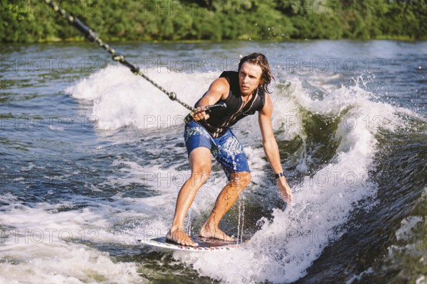 Active wakesurfer jumping on wake board down the river waves. Surfer on wave. Male athlete training on wakesurf training. Active water sports in open air on board. A man catches a wave on surf