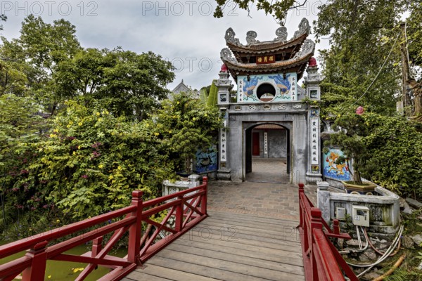 A richly decorated temple with a wooden walkway, surrounded by lush greenery and Asian architectural elements, the Ngoc Son Temple in Hoan Kiem Lake in Hanoi Vietnam