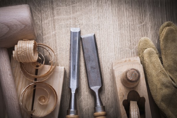 Wooden bricks mallet curled up shavings planer firmer chisels leather gloves on wood background construction concept