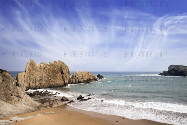 Snow-white sea foam glistens in the dim autumn sun. Cantabria, Spain. Playa de la Arnia beach. Amazing geological formations amaze tourists. Storm waves break on the coastal rocks