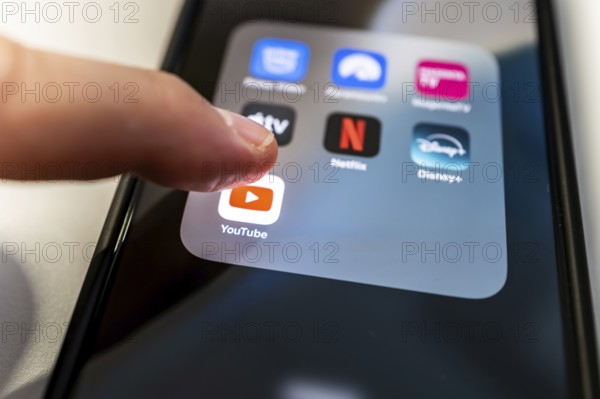 One finger touches the YouTube icon on a smartphone screen with various other streaming apps