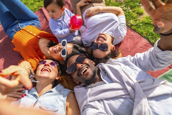 Group of cheerful multi ethnic friends taking a selfie while lying in a circle on a blanket at the park